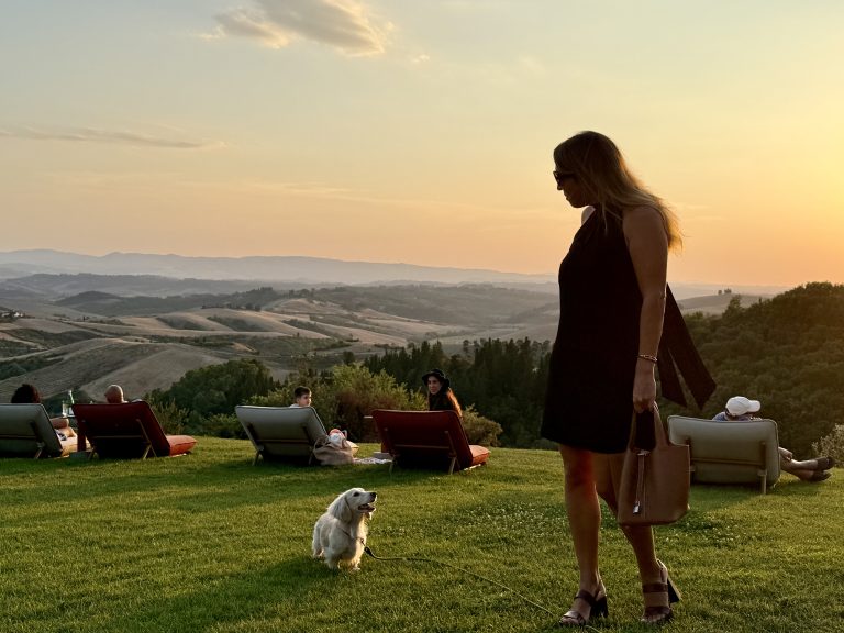 Castelfalfi Tuscany Woman with her small teckel dog (dachshund0 enjoying a vibrant orange sunset over the Tuscany hills, embodying luxury lifestyle travel and mindset of reinvention at 40