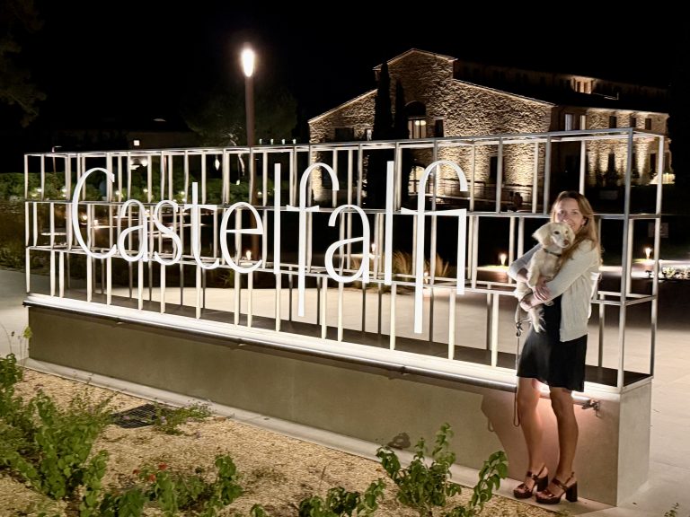 Casltelfalfi Tuscany Woman in her 40s with her cream dachshund in front of the illuminated Castelfalfi sign, representing lifestyle, luxury escapes and personal reinvention