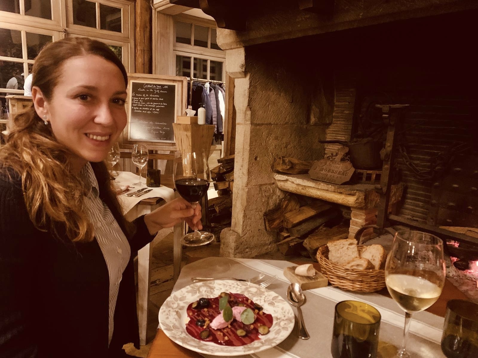 Woman enjoying red wine and gourmet first course by a grand fireplace at La Table du Lavoir, Les Sources de Caudalie.