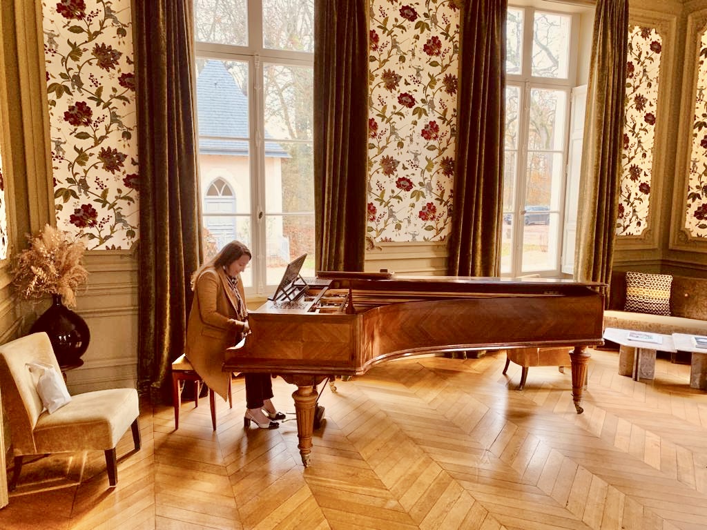 Women playing piano in luxurious salon at castle Les Sources de Cheverny, reflecting luxury lifestyle, travel and personal reinvention at 40s.
